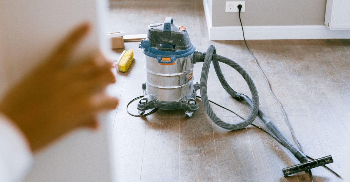 Aspirateur à cuve en inox posé sur un parquet, avec son flexible et sa brosse de sol