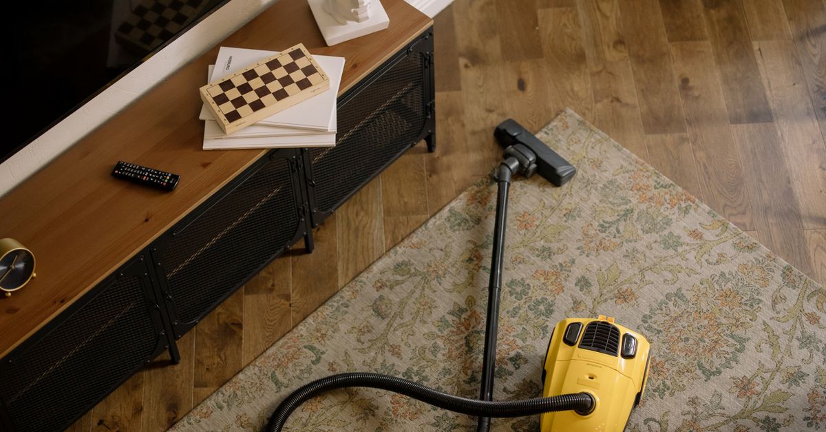 Aspirateur traîneau jaune posé sur un tapis à motifs floraux, devant un meuble télé