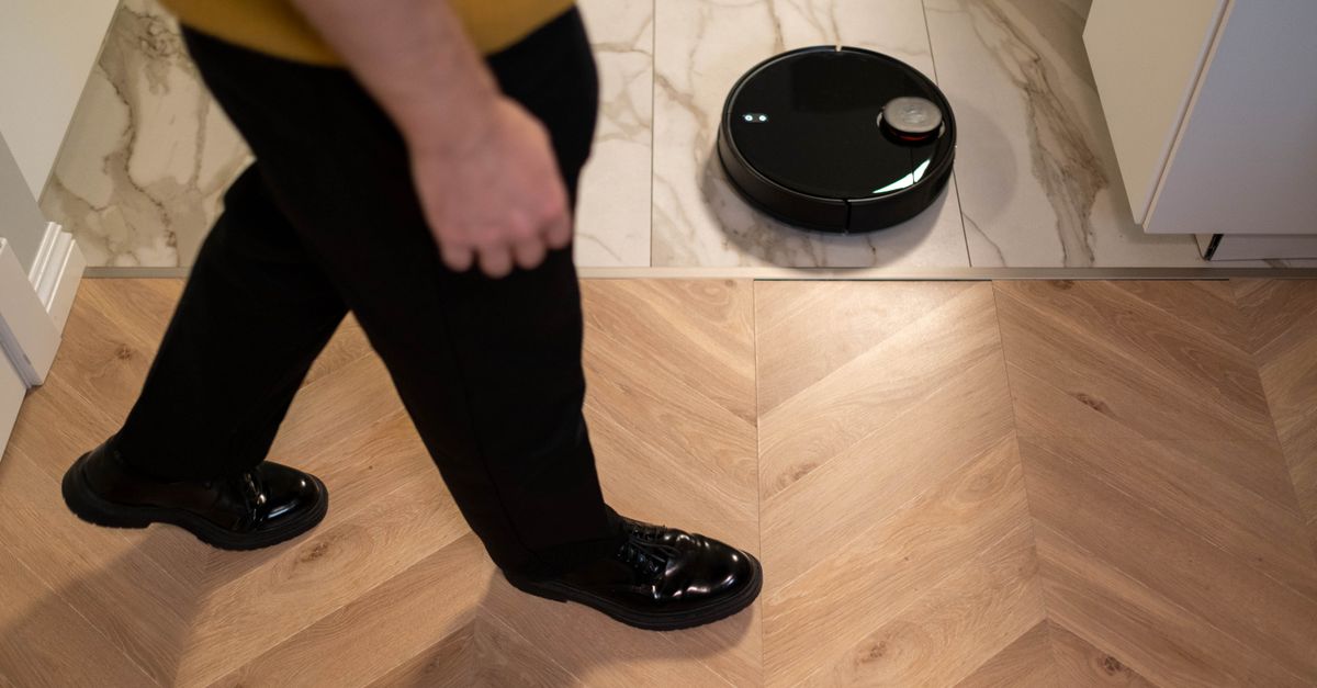 Robot aspirateur noir sur un carrelage, près d'une personne qui marche sur un parquet